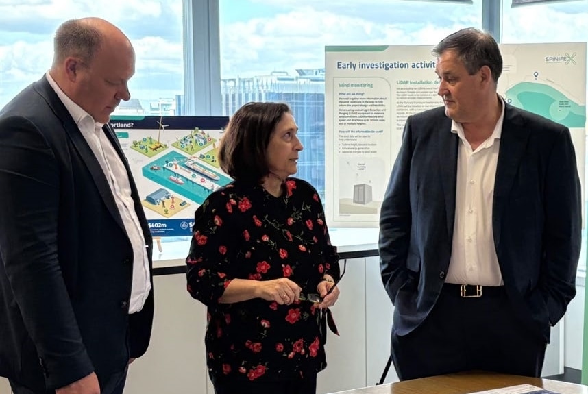 An image of Alinta Energy CDO Andres Maasing (left), Victorian Energy Minister Lily D'Ambrosio (centre), and Alinta Energy CEO Jeff Dimery.  They are standing in an office setting. Behind them are materials related to the Spinifex Offshore Wind Project and large windows showing a cityscape behind them.